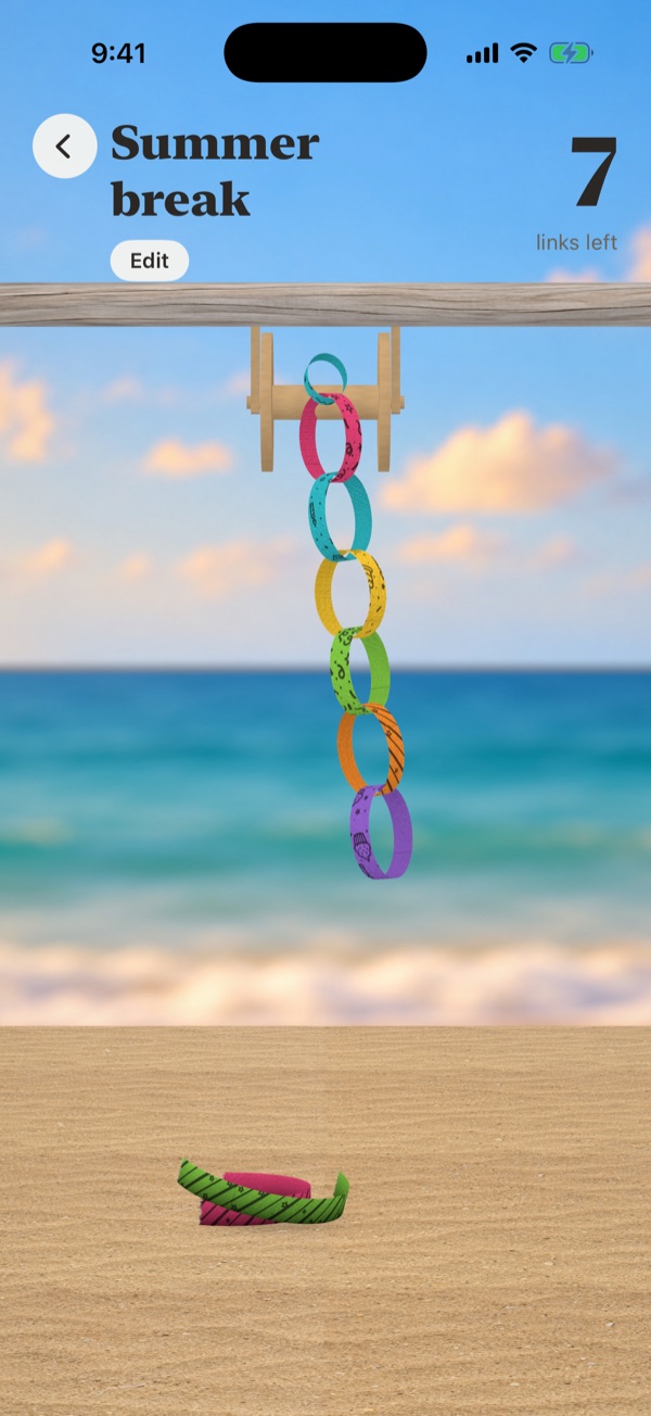 A bright paper chain hanging from driftwood at the beach, with the sea behind it